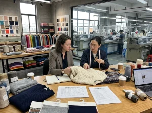 Brand buyer and factory team reviewing sweater samples, yarn swatches, and sourcing documents inside a modern knitwear factory in China.