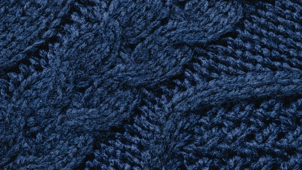 Dark blue cable knit sweater texture with dense yarn structure and raised stitch pattern