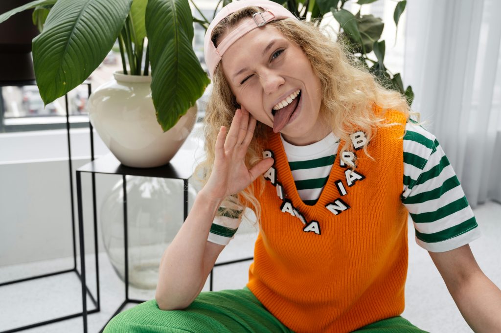 Woman wearing bright orange custom vest knitwear layered over a striped T-shirt