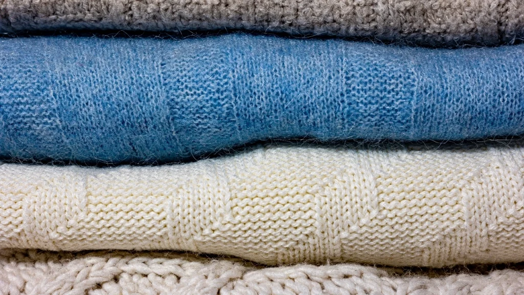 Bulk knit sweaters close-up showing layered blue, cream, and beige knitted fabric textures.