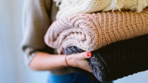 Bulk knit sweaters folded and carried by hand, showing soft textures and neutral winter colors.