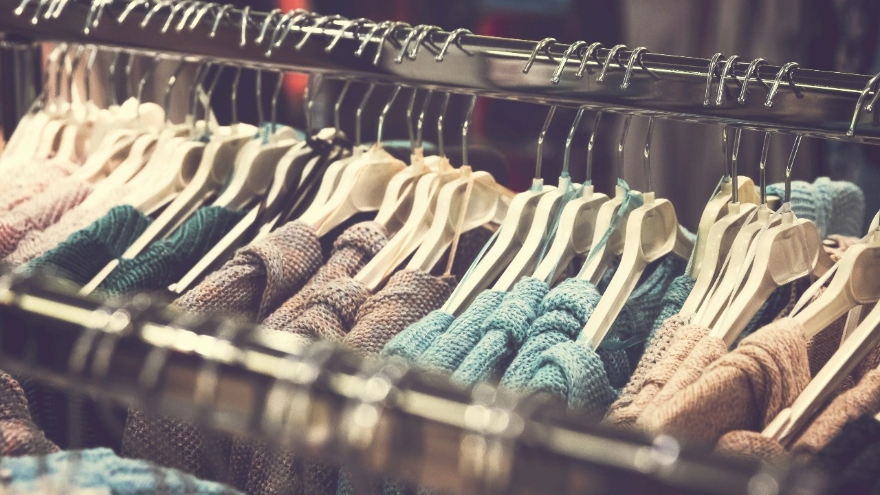 Bulk knit sweaters hanging on a retail rack with soft colors and textured knit patterns.