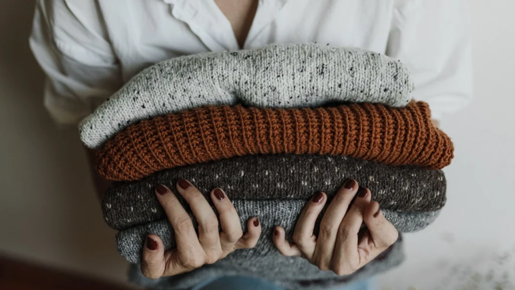 Bulk knit sweaters stacked in neutral and earthy colors with visible ribbed knit texture.