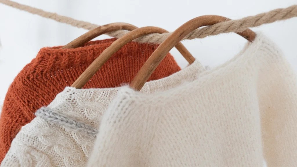 Cardigan Sweater collection hanging on wooden hangers with cream, cable knit, and rust knit styles.