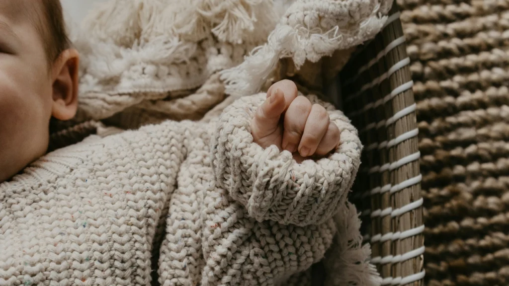 Baby wearing a cream chunky knit cardigan with textured stitches and ribbed cuffs
