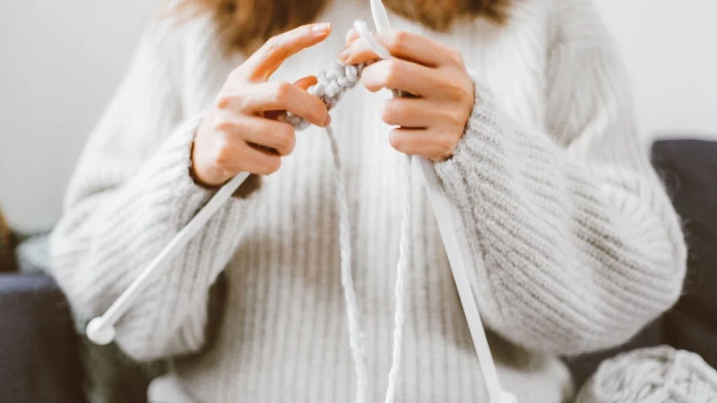 Woman wearing a chunky knit cardigan while working with thick yarn and knitting needles