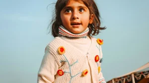 Child wearing a cream embroidered cardigan with colorful floral details and textured knit structure