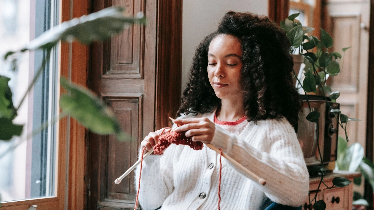 Woman knitting yarn while wearing a white cardigan for custom cardigans embroidered development