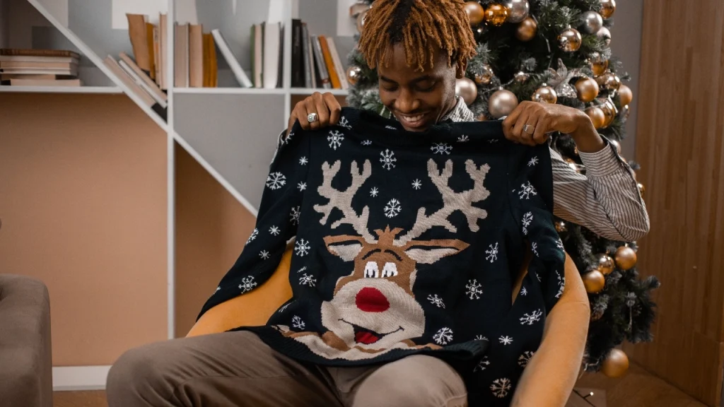 Man holding a black reindeer Christmas sweater for custom embroidered sweaters design reference