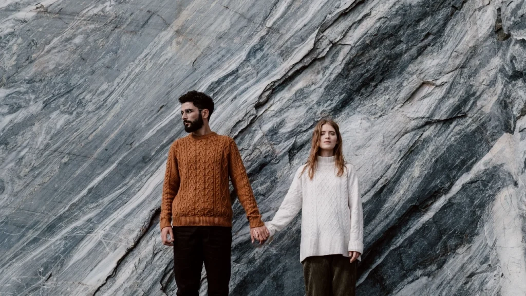Custom Knit Sweaters worn by a couple in cable knit styles against a marble stone background.