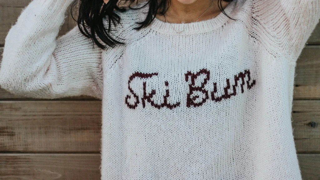 Custom Knit Sweaters cream pullover with knitted lettering on the front.