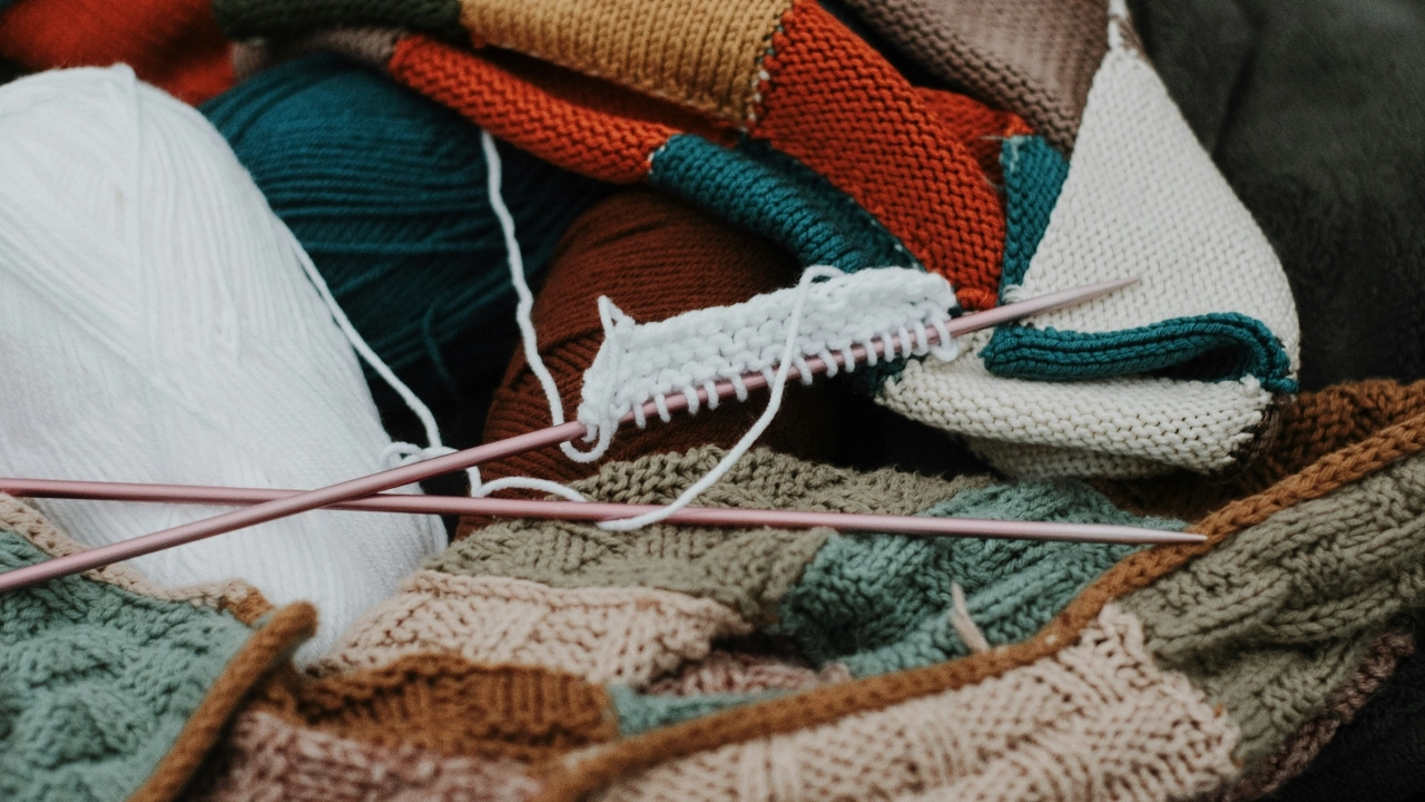 Custom Knit Sweaters in progress with yarn, knitting needles, and mixed knit textures for handmade sweater development.