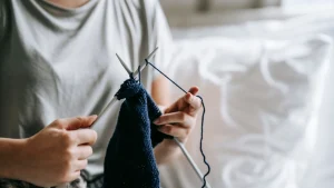 Custom knitwear hand knitting process with blue yarn and needles in a soft indoor setting.