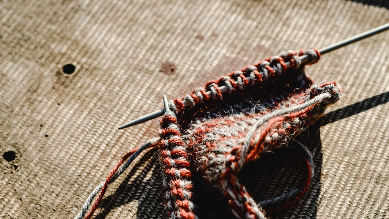 Custom knitwear swatch on knitting needles showing yarn texture and handmade stitch development.