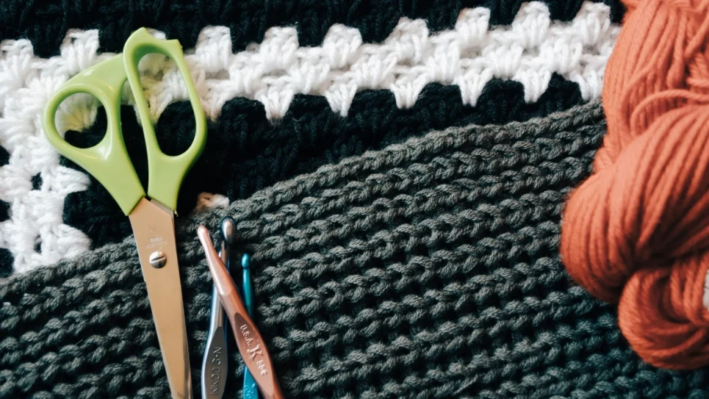 Custom knitwear tools with scissors, crochet hooks, yarn, and textured knitted fabric for design preparation.