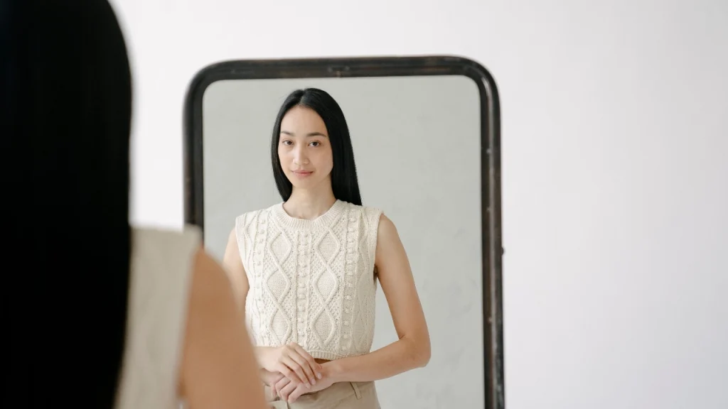 Woman viewing cream custom vest knitwear with cable patterns in a full-length mirror