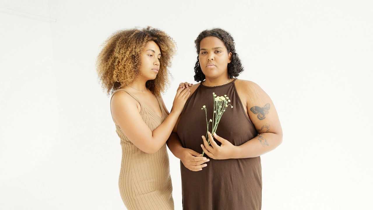 Two women wearing neutral ribbed knit dresses in a minimal studio setting.