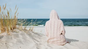 Person wearing a light pink cable knit hoodie while sitting on a beach