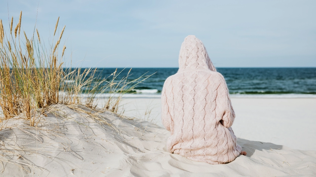 Person wearing a light pink cable knit hoodie while sitting on a beach
