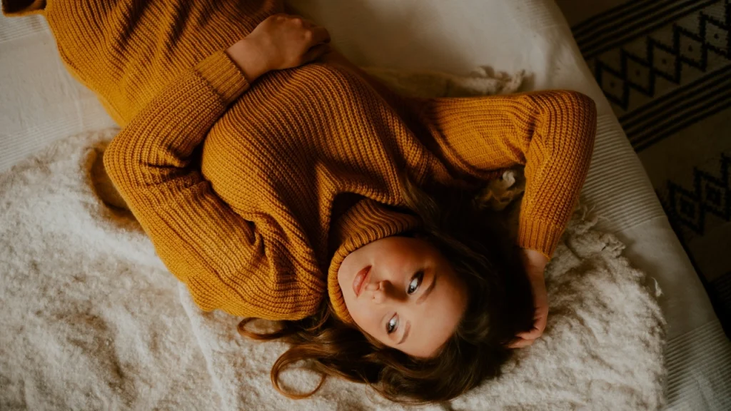 Woman wearing a mustard knit maxi dress with a turtleneck while lying on a soft bed