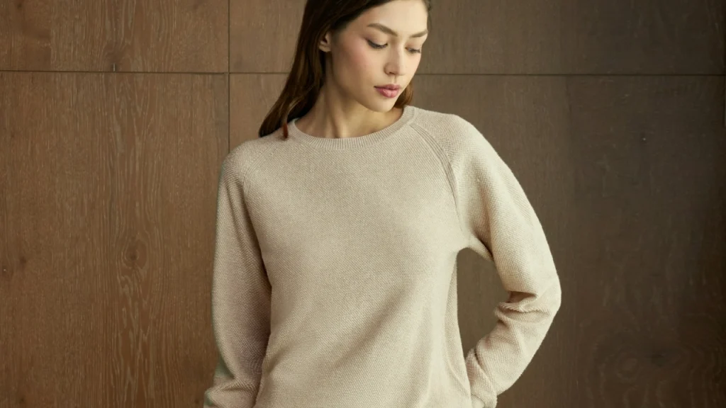Model wearing a cream knit sweater dress in a clean studio setting with a wooden background.