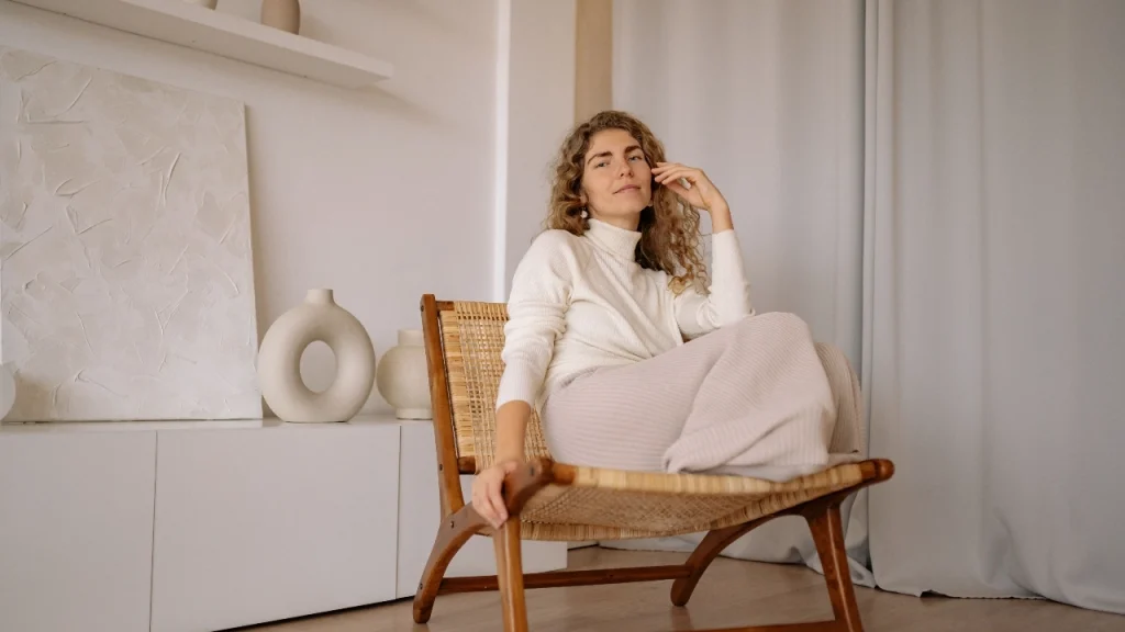 Woman wearing a cream turtleneck knit sweater dress while seated in a soft neutral interior.