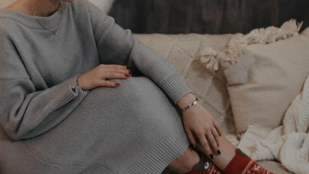 Woman wearing a gray knit sweater dress while seated on a soft indoor sofa.