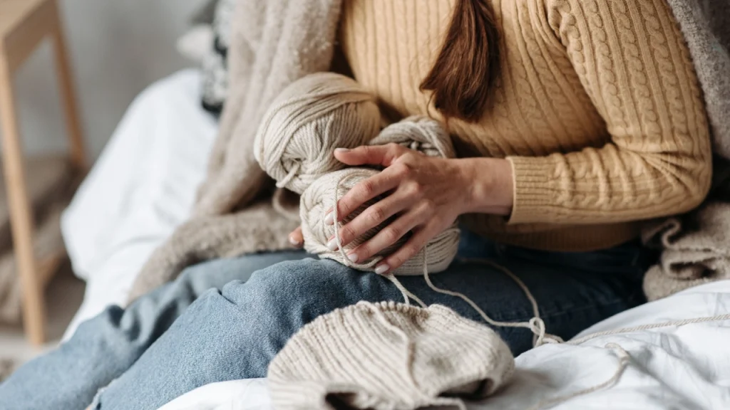 Hands holding yarn balls while wearing a cable knit sweater for knitted sweater manufacturer development