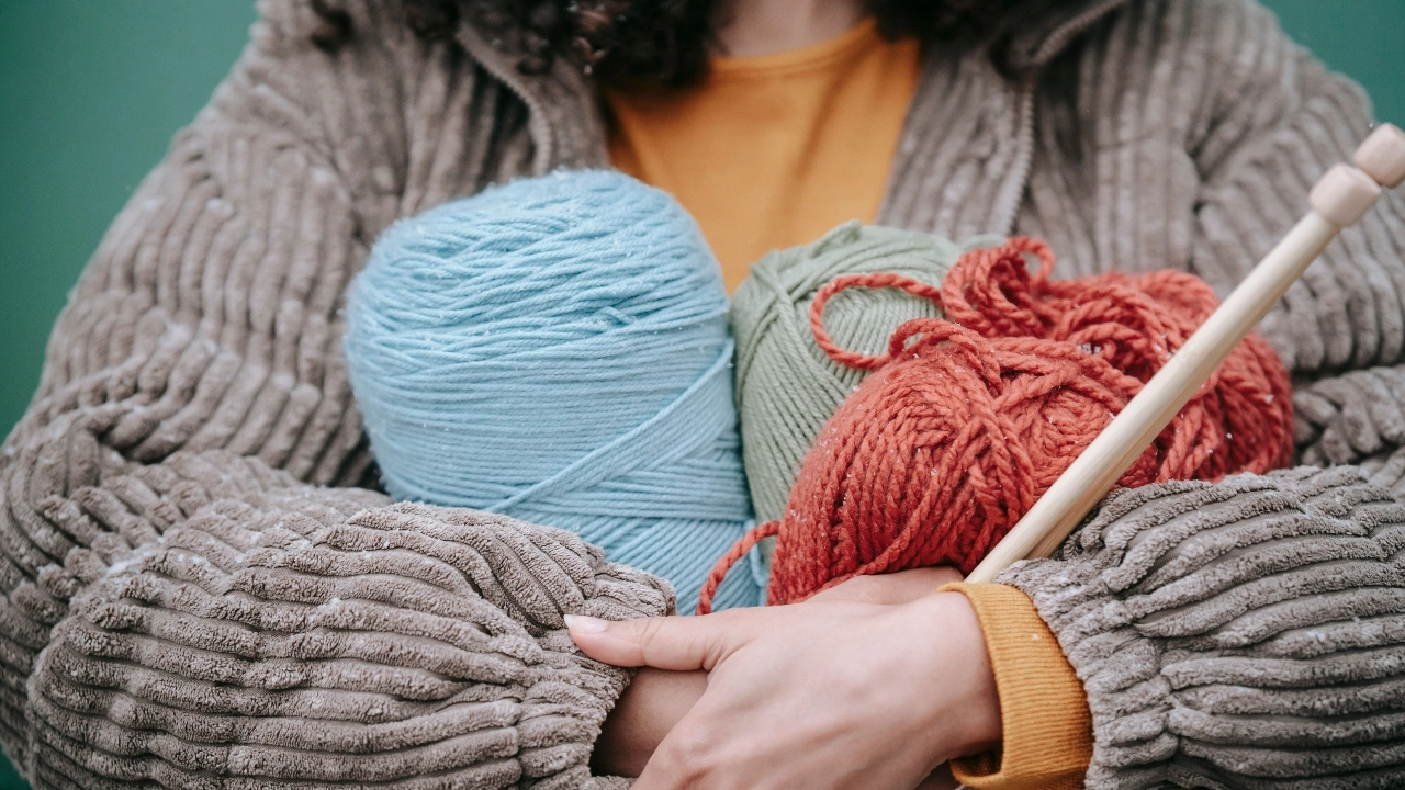 Person holding colorful yarn balls and knitting needles for knitted sweater manufacturer material development