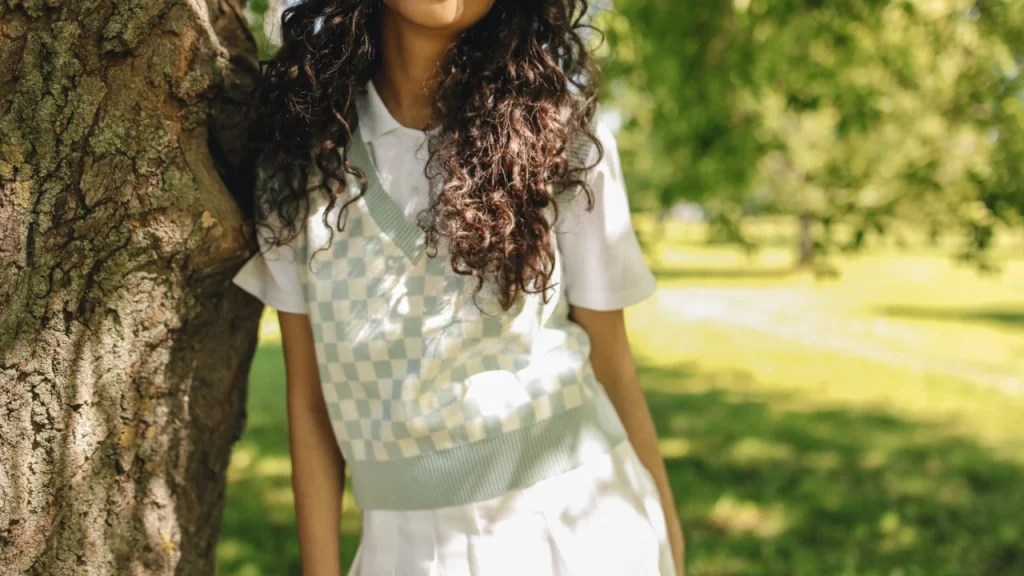 Woman wearing a pastel checkerboard knitted V-neck vest over a white polo shirt outdoors