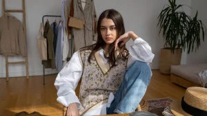 Woman wearing a floral knitted V-neck vest over an oversized white blouse indoors
