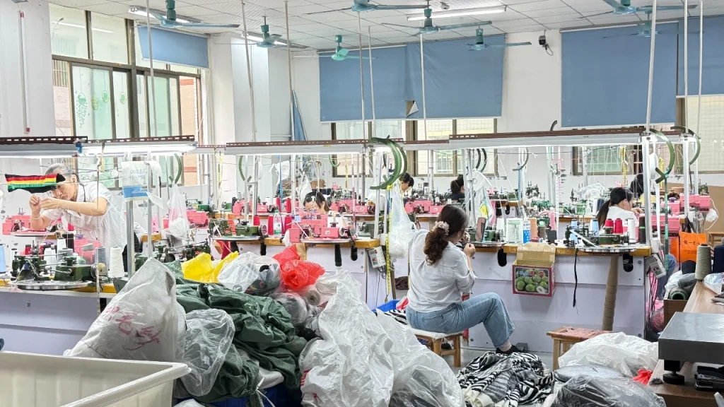 Knitwear factory sewing workshop with workers handling garment production and finishing tasks