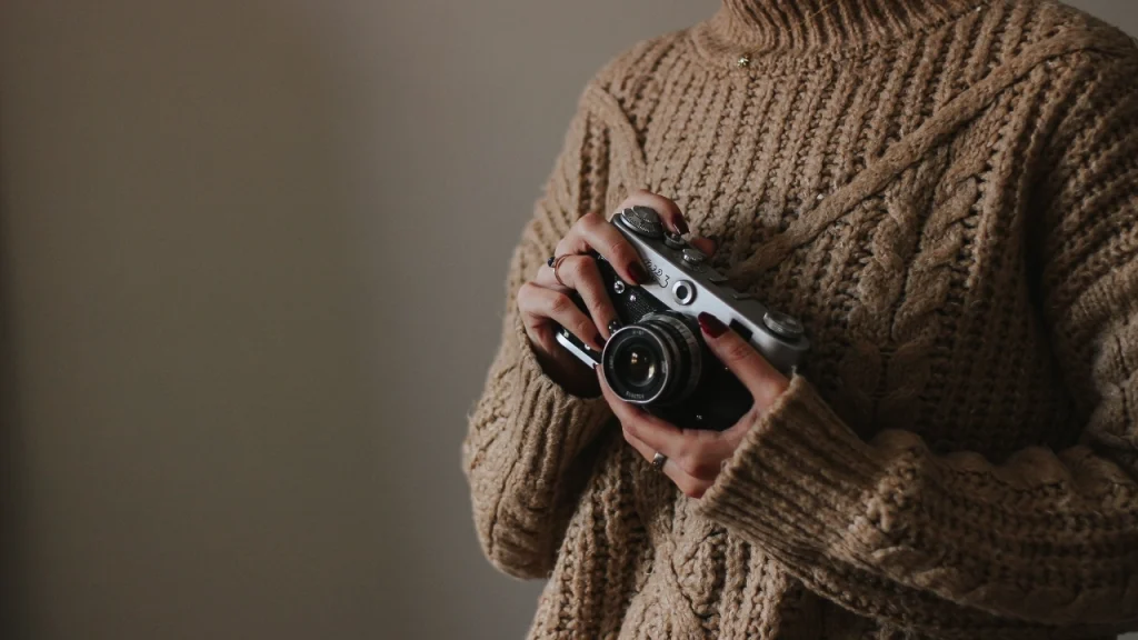 Knitwear Manufacturer chunky cable sweater shown with a camera in a warm indoor setting.