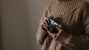 Knitwear Manufacturer chunky cable sweater shown with a camera in a warm indoor setting.