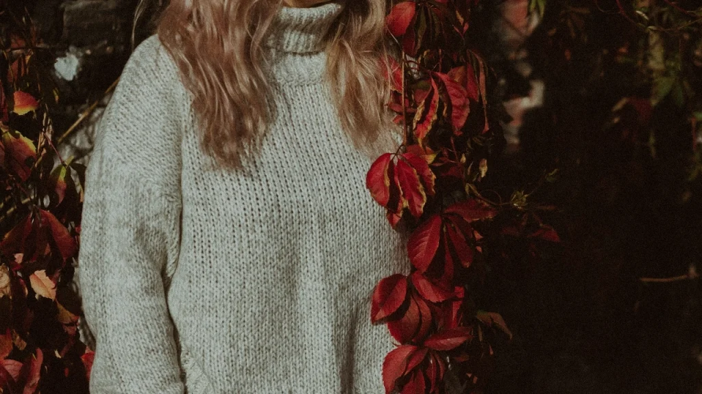 Knitwear Manufacturer cream sweater styled outdoors with autumn red leaves.