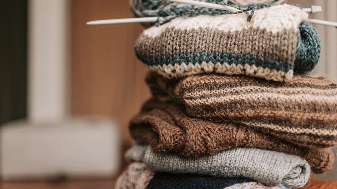 Knitwear Manufacturer folded knitwear samples with knitting needles and layered textures.