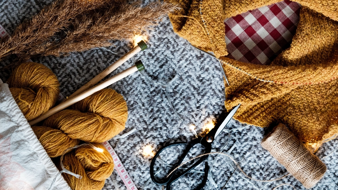 Knitwear Manufacturer yarn, knitting needles, scissors, measuring tape, and fabric arranged for sweater production planning.