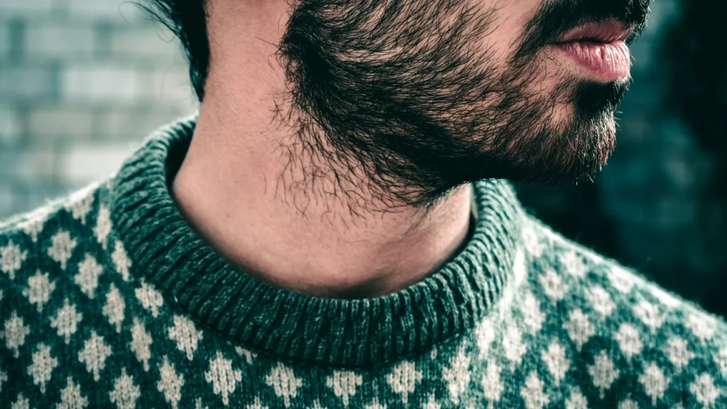 Close-up of a green patterned sweater neckline, showing detailed Mens Knitwear texture and jacquard design.