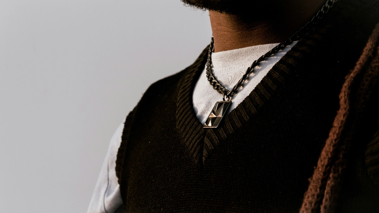 Close-up of a black mens sleeveless jumper layered over a white T-shirt with chain accessories.