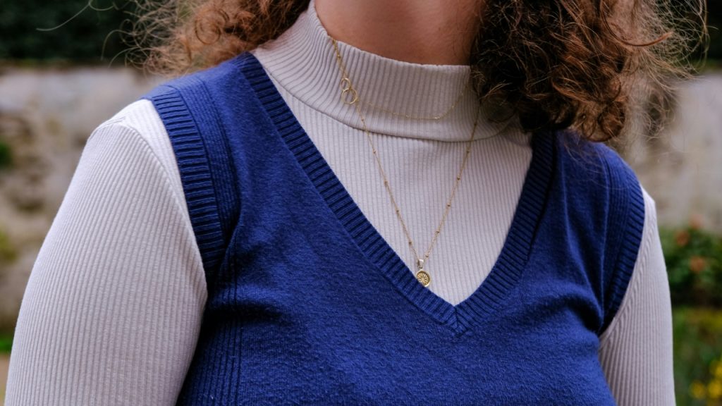 Blue V-neck sleeveless jumper layered over a white ribbed turtleneck