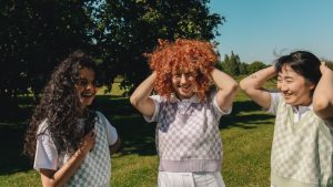 Three models wearing pastel checkerboard sleeveless jumpers in an outdoor park