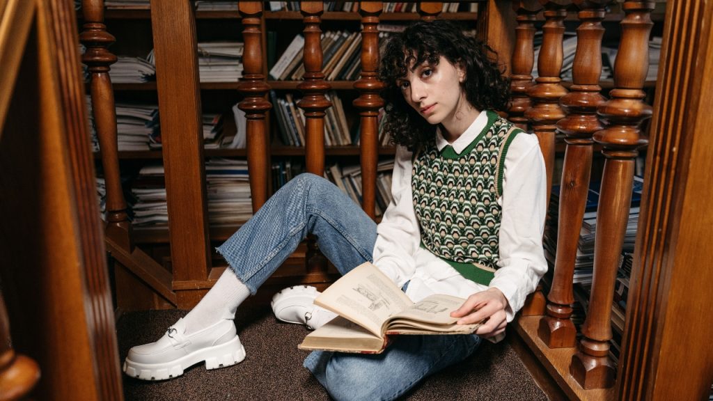 Woman wearing a green patterned sleeveless jumper over a white shirt while reading