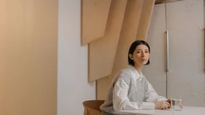 Woman wearing grey sleeveless knitwear over a white collared shirt in a minimalist interior
