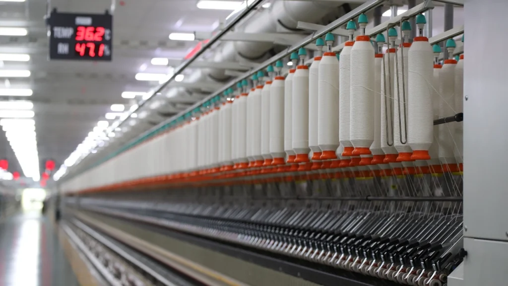 Sweater Factory industrial yarn production line with white yarn cones in a large textile workshop.