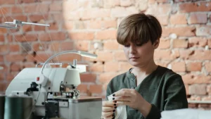 Sweater Factory worker preparing knitwear details beside an industrial sewing machine in a production workshop.