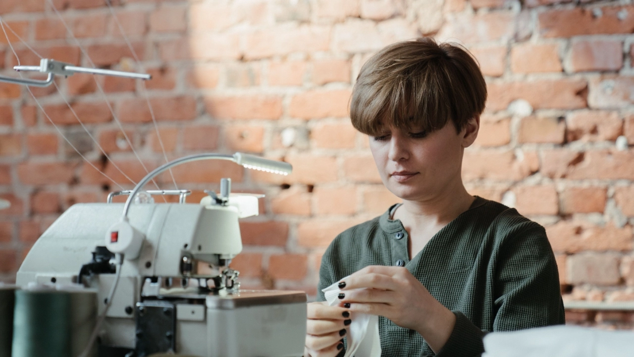 Sweater Factory worker preparing knitwear details beside an industrial sewing machine in a production workshop.