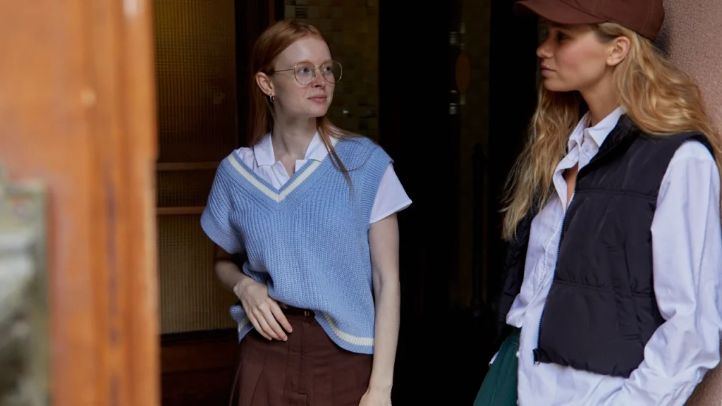 Woman wearing a light blue sweater vest with contrast V-neck trim over a white polo shirt