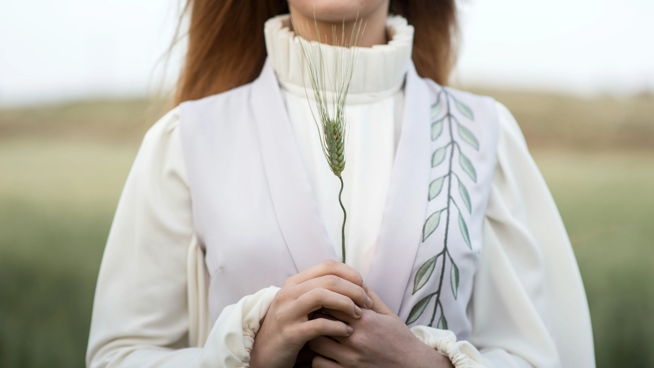 Soft neutral sweater vest styled over a high-neck blouse in an outdoor natural setting