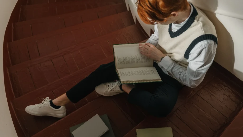 Person wearing a cream V-neck sweater vest over a white shirt while reading indoors