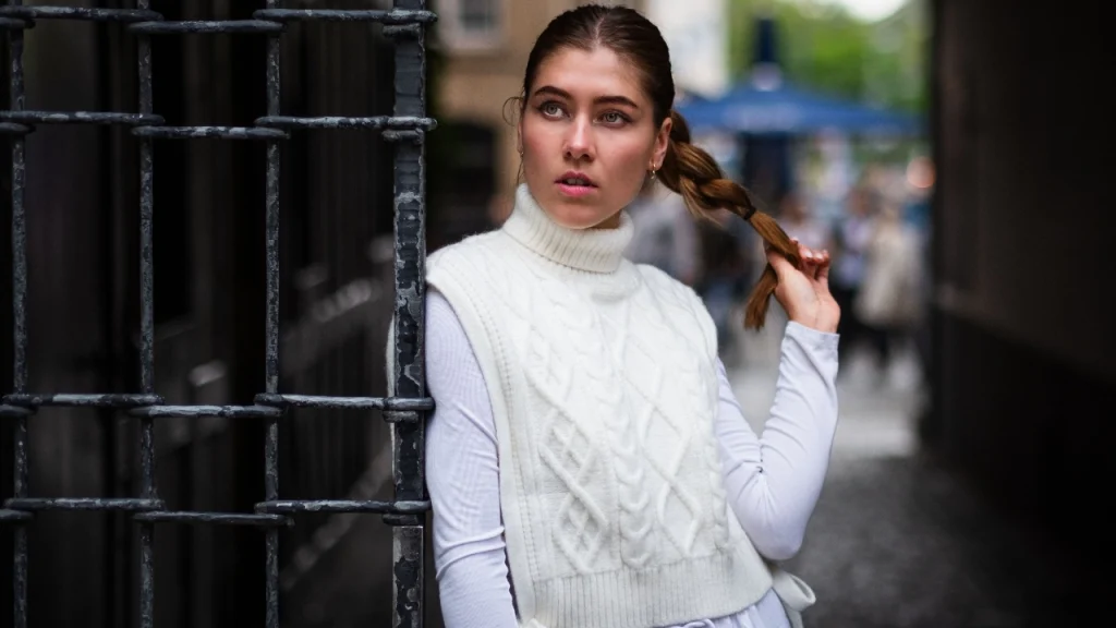 Woman wearing a white cable-knit sweater vest with a high turtleneck and ribbed hem